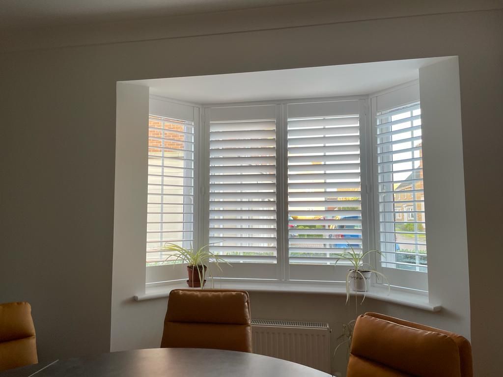 A dining room with a table and chairs and a bay window with shutters.