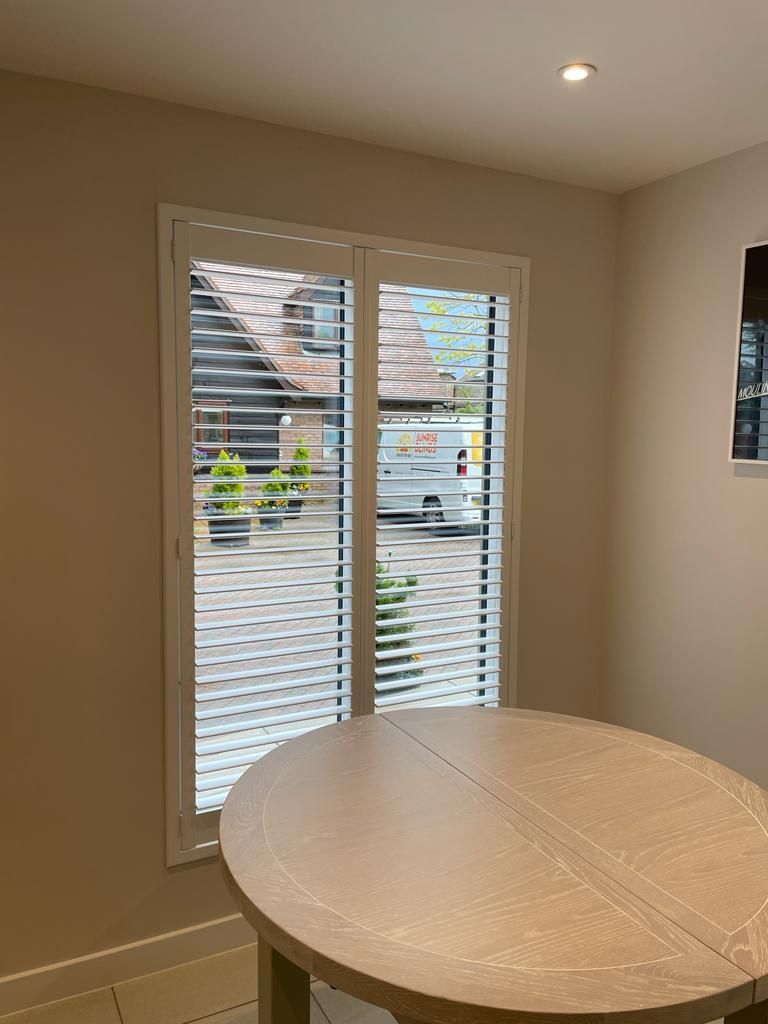 A kitchen with a round table and shutters on the windows.