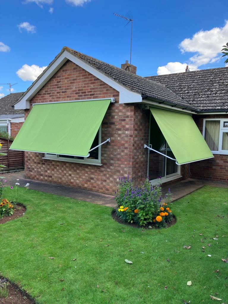 A brick house with a green awning on the windows.