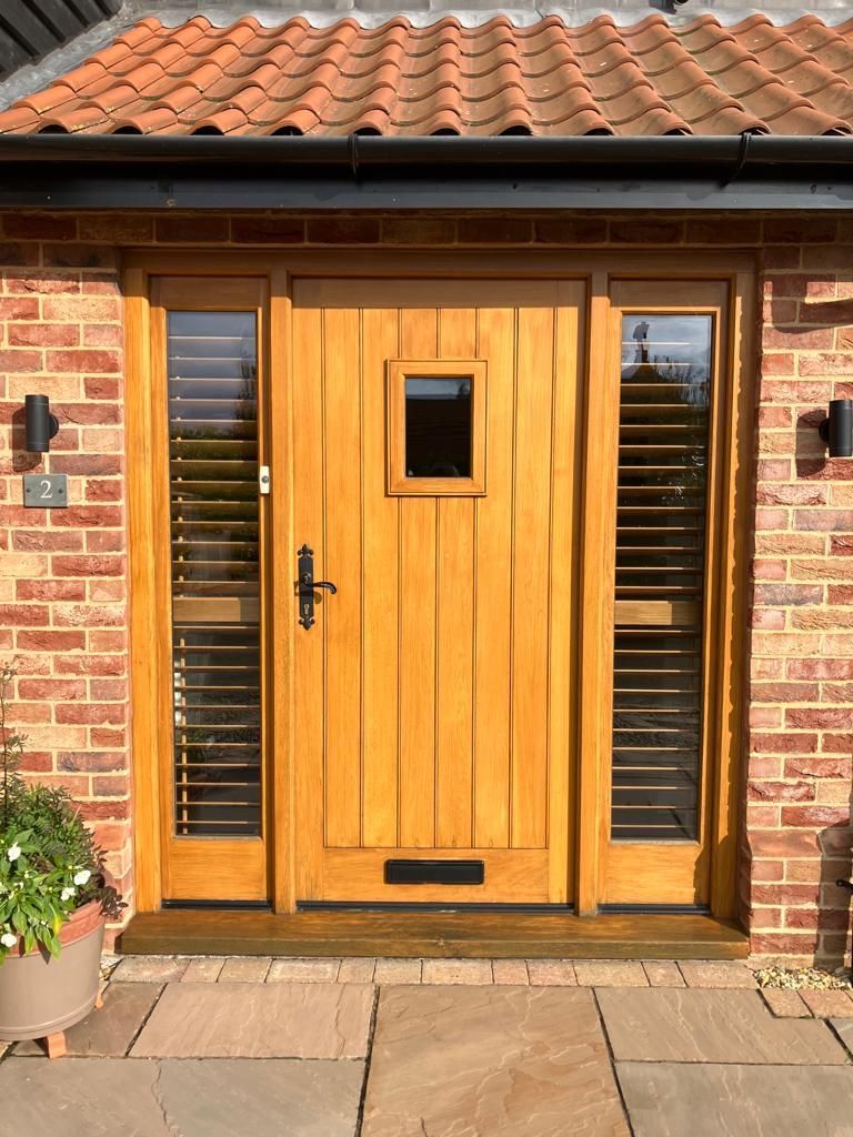 The front door of a brick house with a wooden door and shutters.
