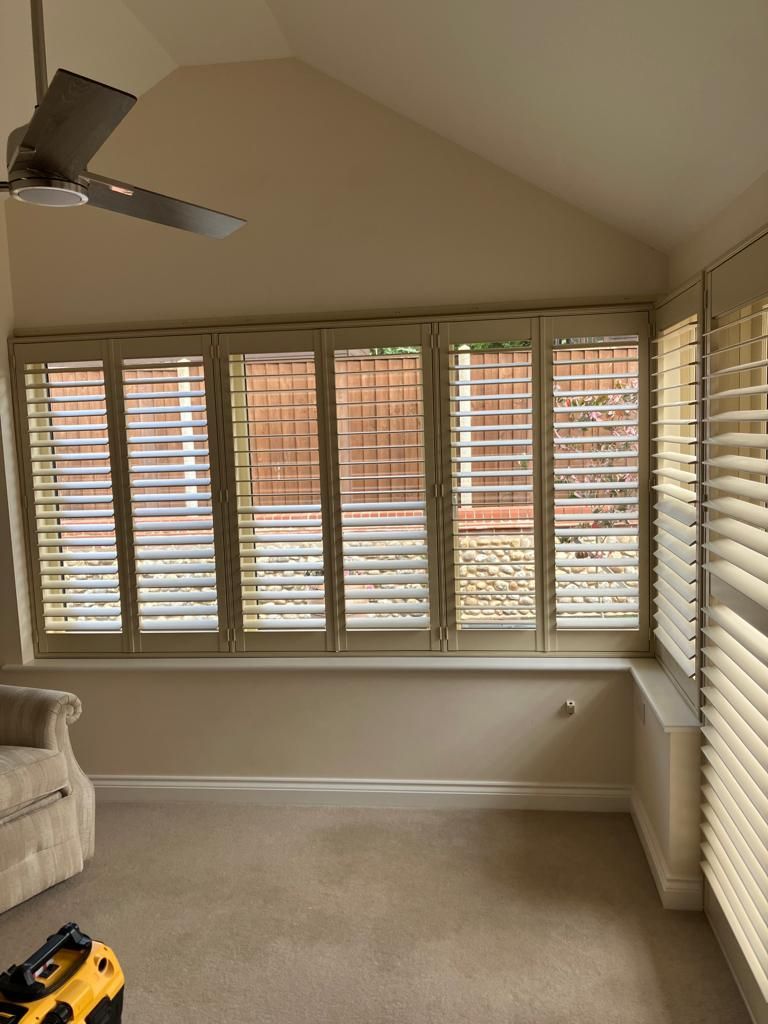 There is a ceiling fan in the room with shutters on the windows.