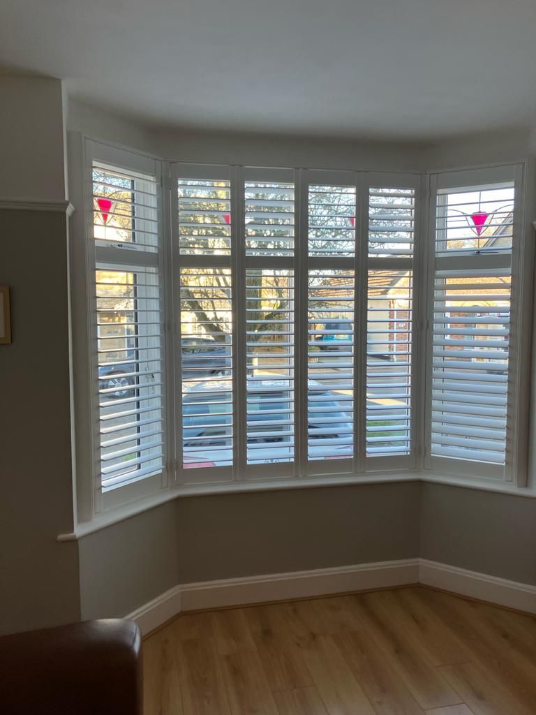 A living room with a large bay window with shutters on it.