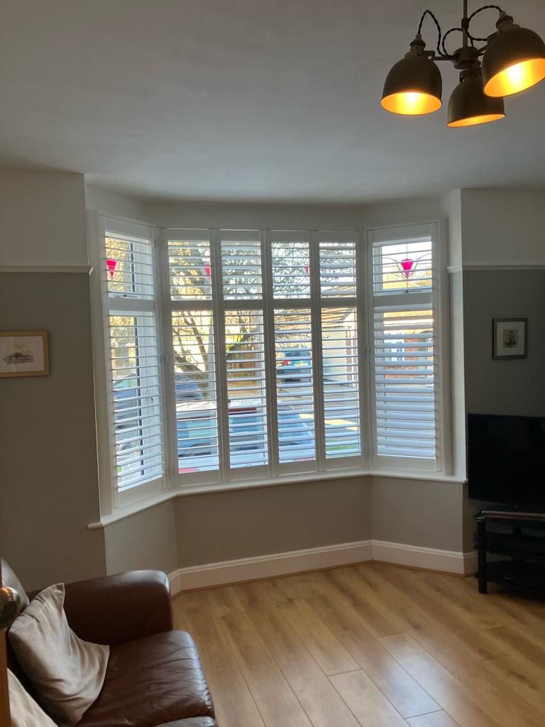 A living room with a couch and a large window with shutters.