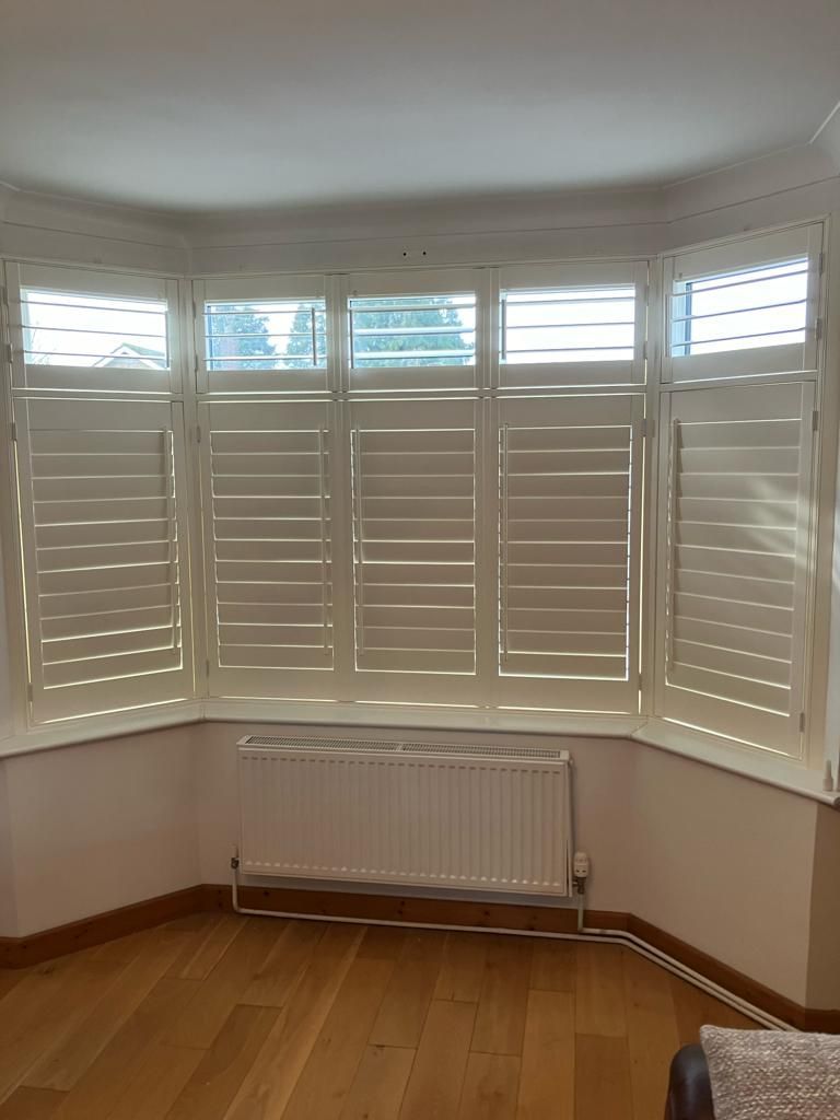 A living room with white shutters on the windows and a radiator.