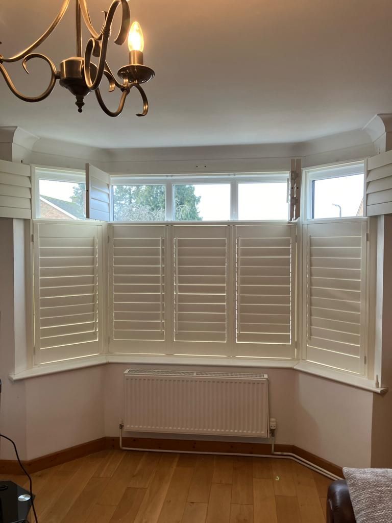 A living room with white shutters on the windows and a chandelier.