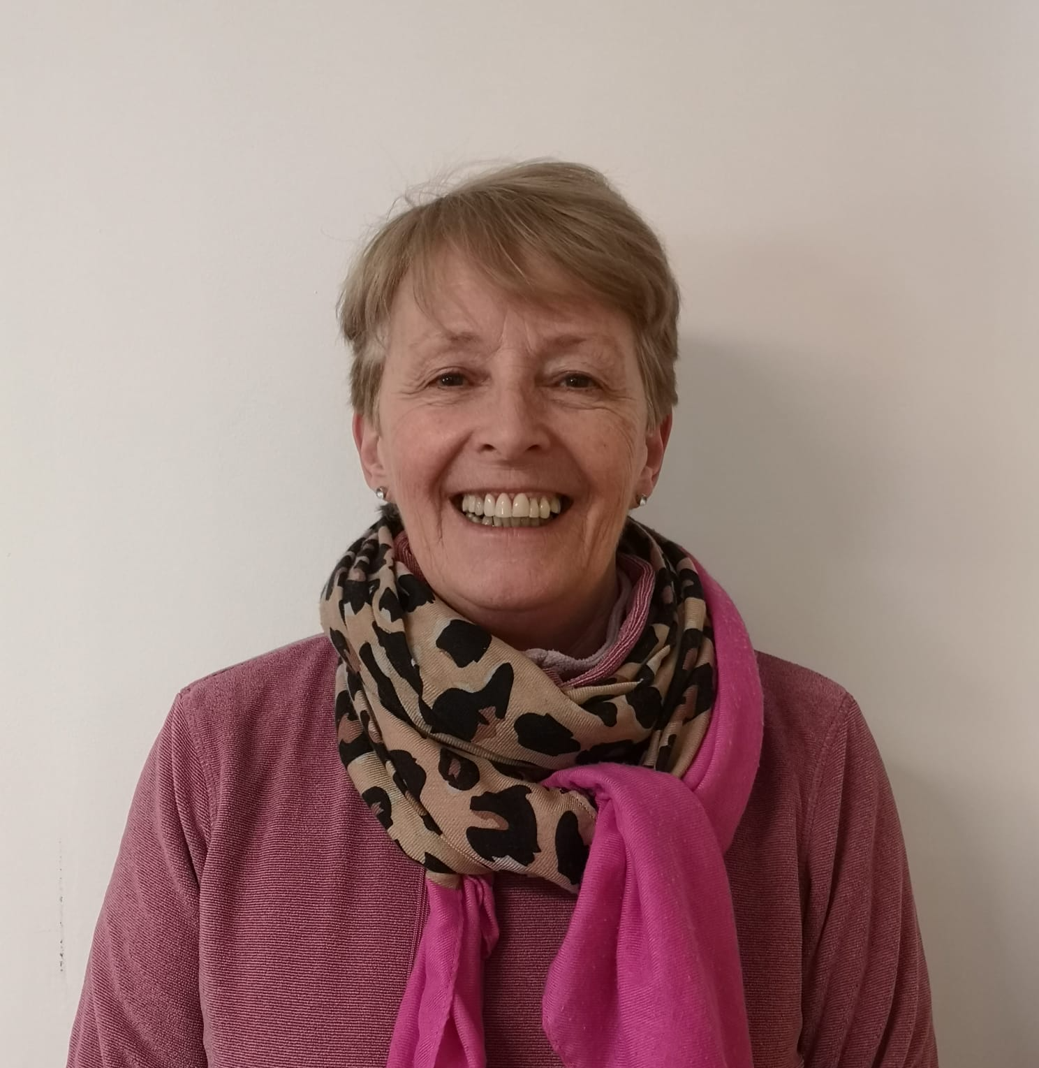 A woman wearing a pink sweater and a leopard print scarf is smiling