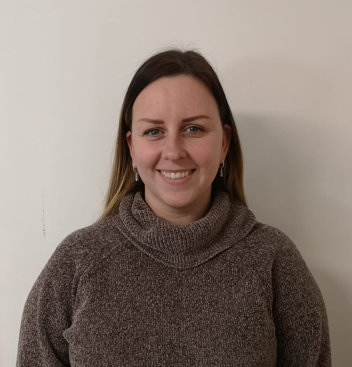 A woman in a brown sweater is smiling for the camera.