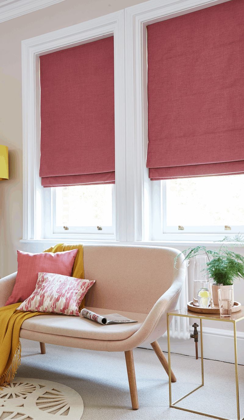 A living room with a couch and two windows with pink blinds.