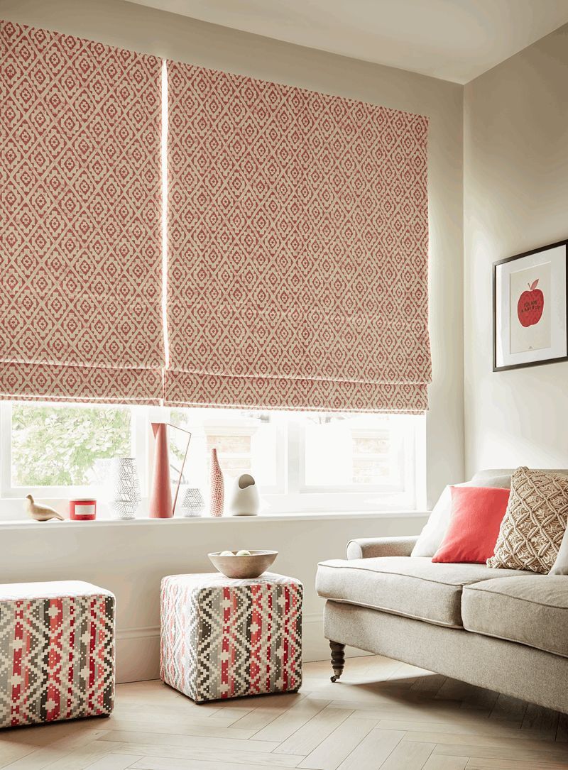 A living room with a couch , ottomans , and a window with roman blinds.