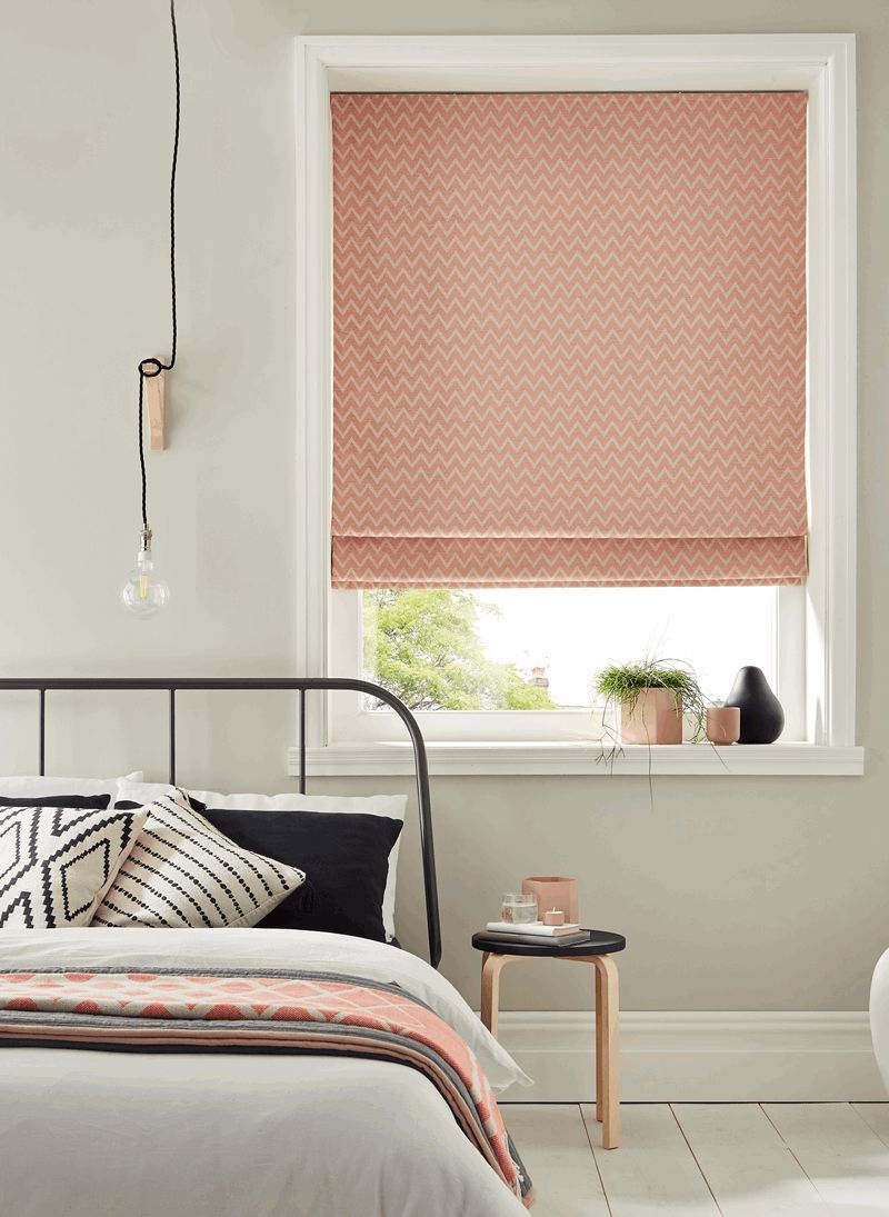 A bedroom with a bed and a window with a pink roman blind.