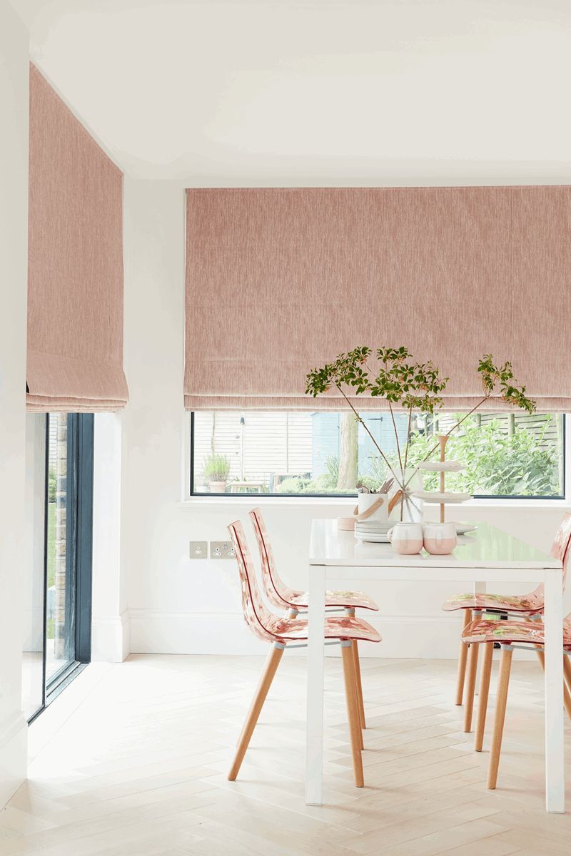 A dining room with a table and chairs and a window with pink blinds.