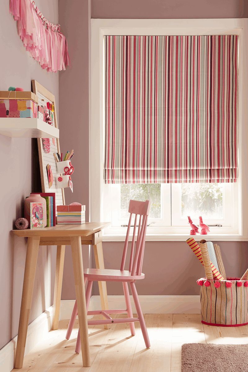 A child 's room with a desk , chair , and window with a pink striped blind.