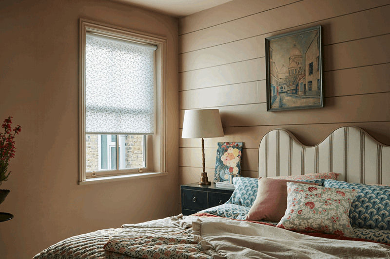 A bedroom with a bed , nightstand , lamp and window.