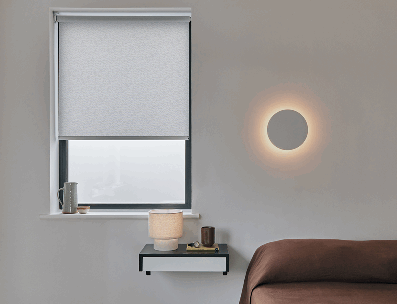 A bedroom with a bed , nightstand , lamp and window.