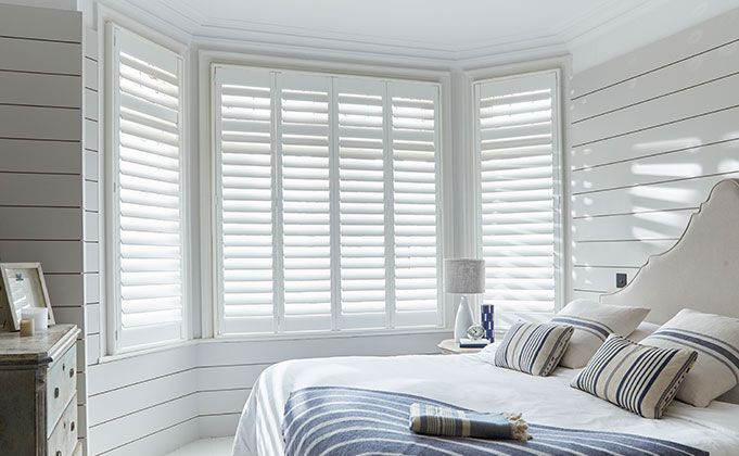A living room with a couch , chair , table and window with white shutters.
