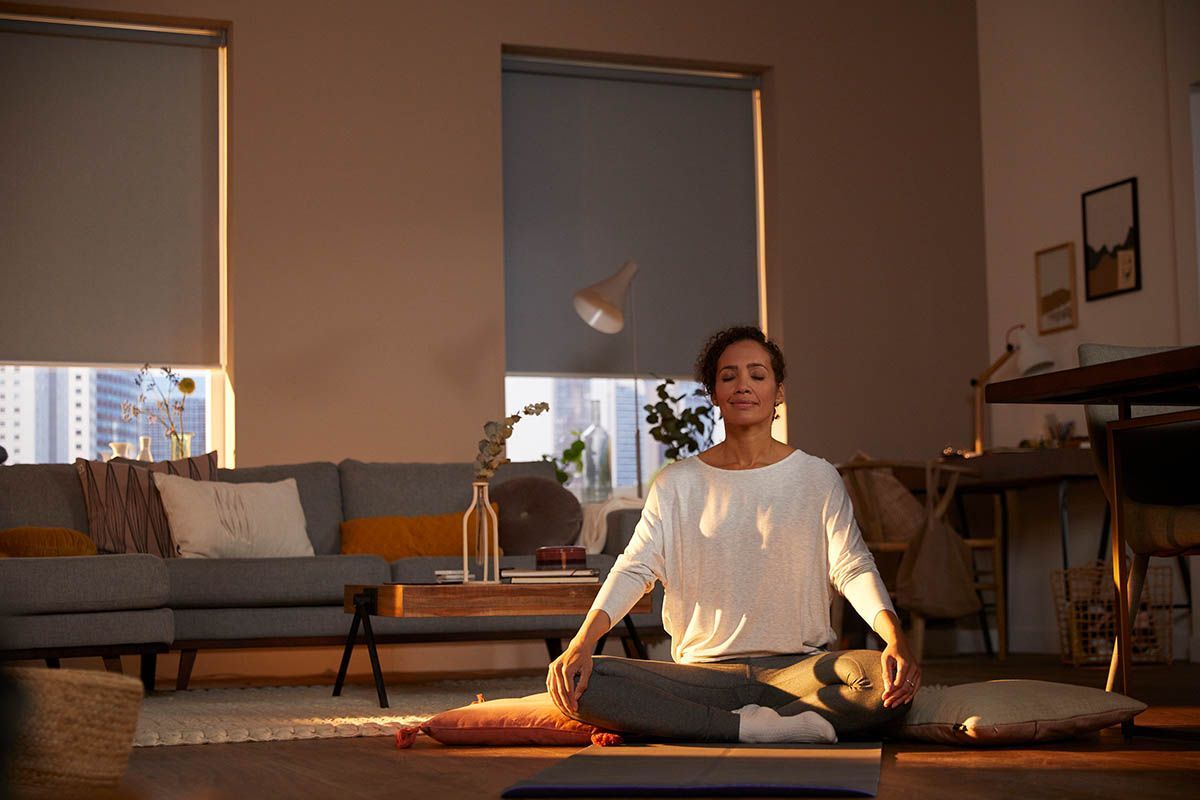 A woman is sitting on a yoga mat in a living room.
