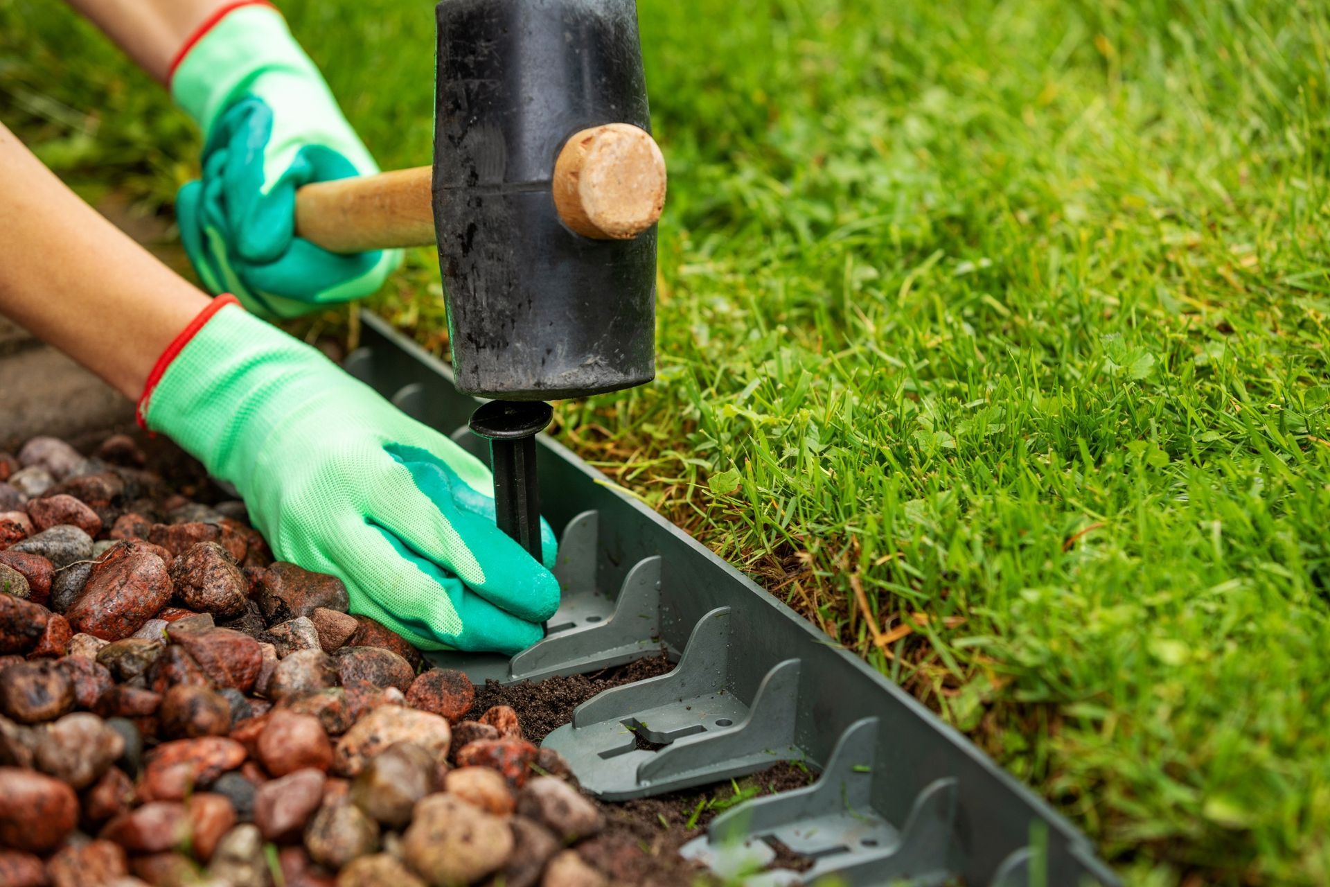 Person wearing green gloves uses a mallet to install a plastic lawn edging.