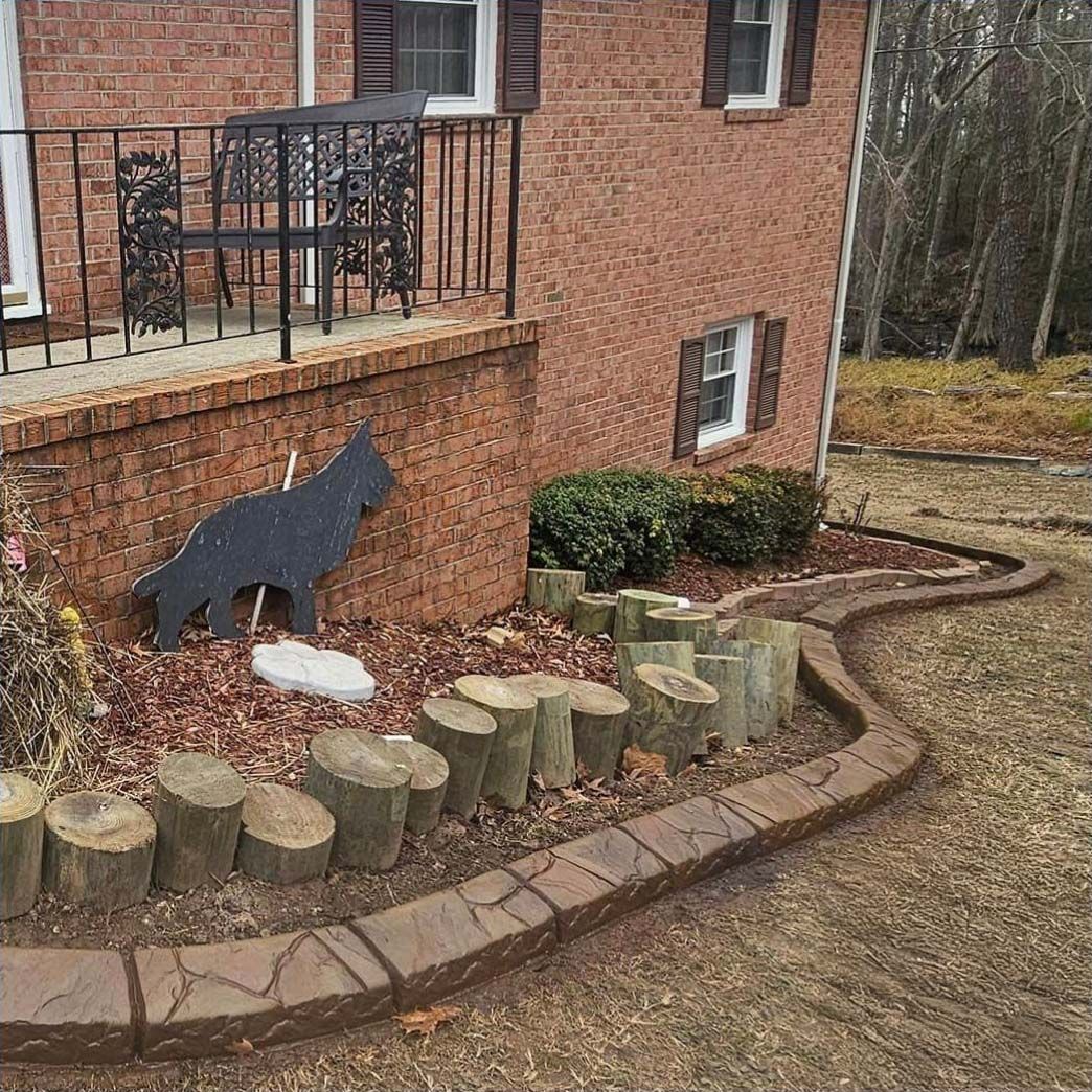 Red brick house with a front yard. Landscaped with tree stumps and a concrete border. Silhouette of a dog.