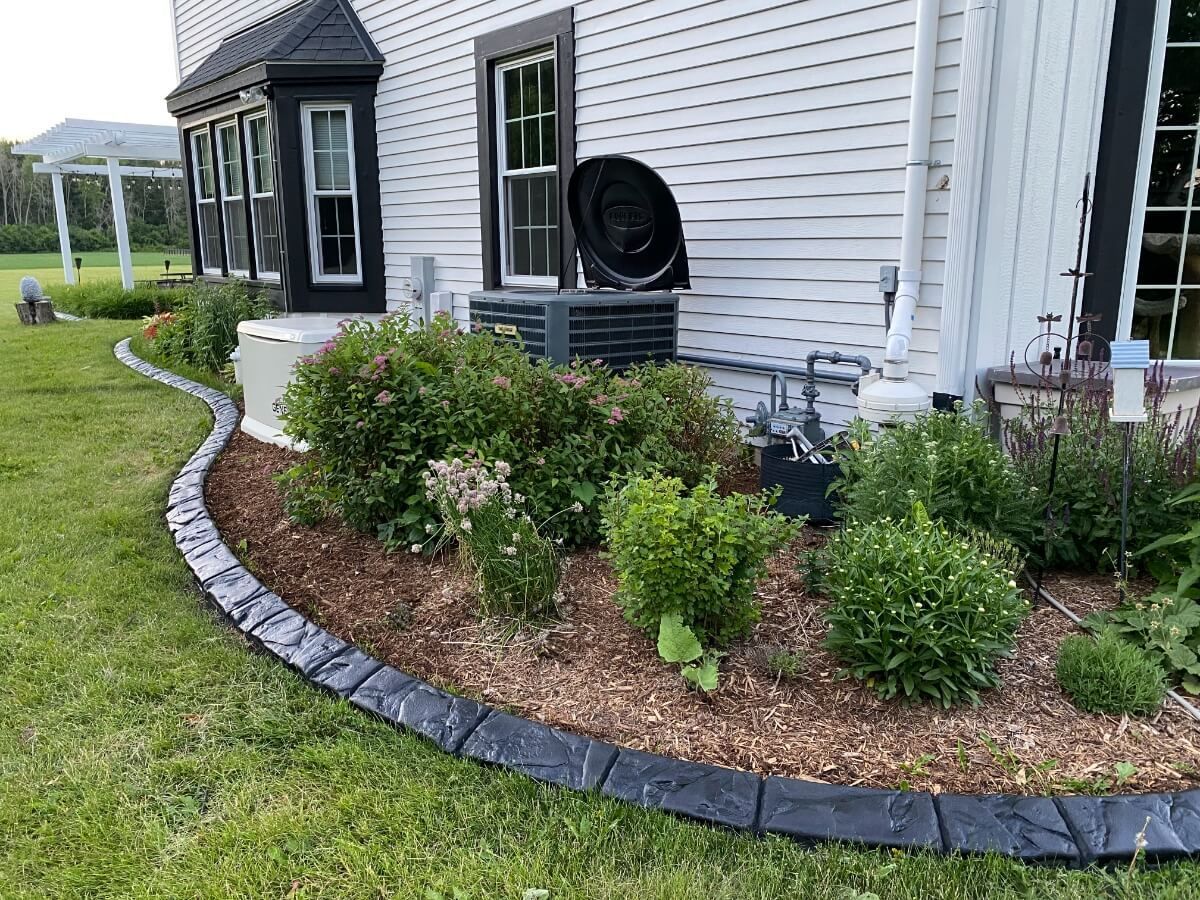 Landscaped house exterior with flower bed, wooden mulch, and gray stone edging.