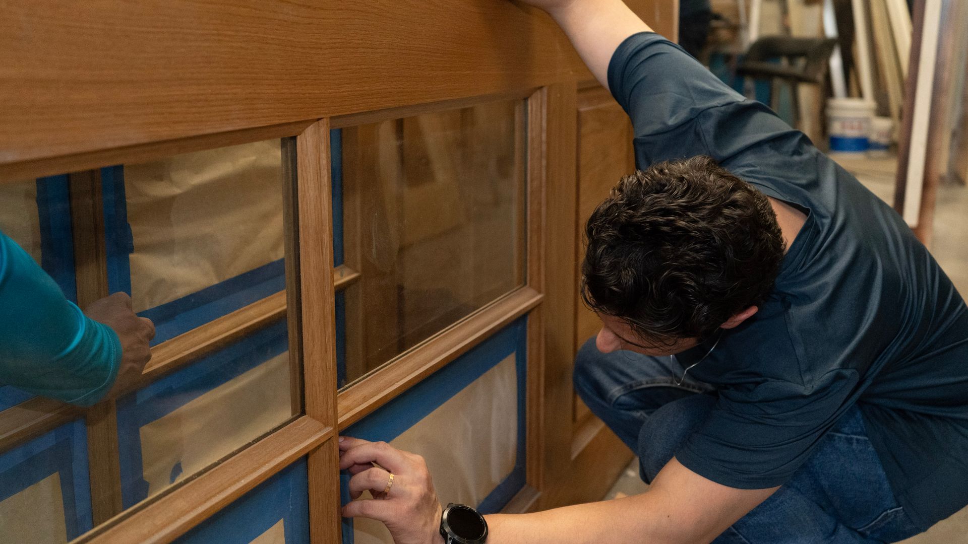 Man working with wood in a workshop, saws and wood pieces visible.