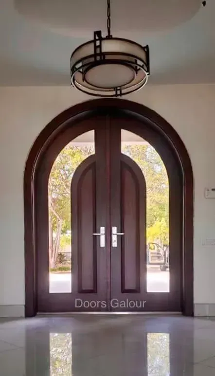 Dark wood double arched doors with glass panels; round light fixture above.