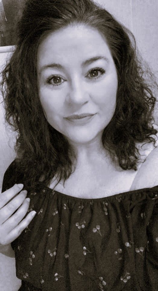 A woman is sitting on a rock next to a stream in the woods.