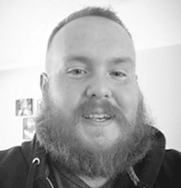 A man with a beard is smiling in a black and white photo.