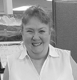A woman in a white shirt is smiling in a black and white photo.