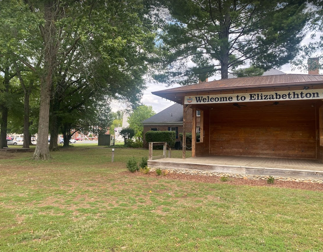 A wooden building in the middle of a grassy field with trees in the background.