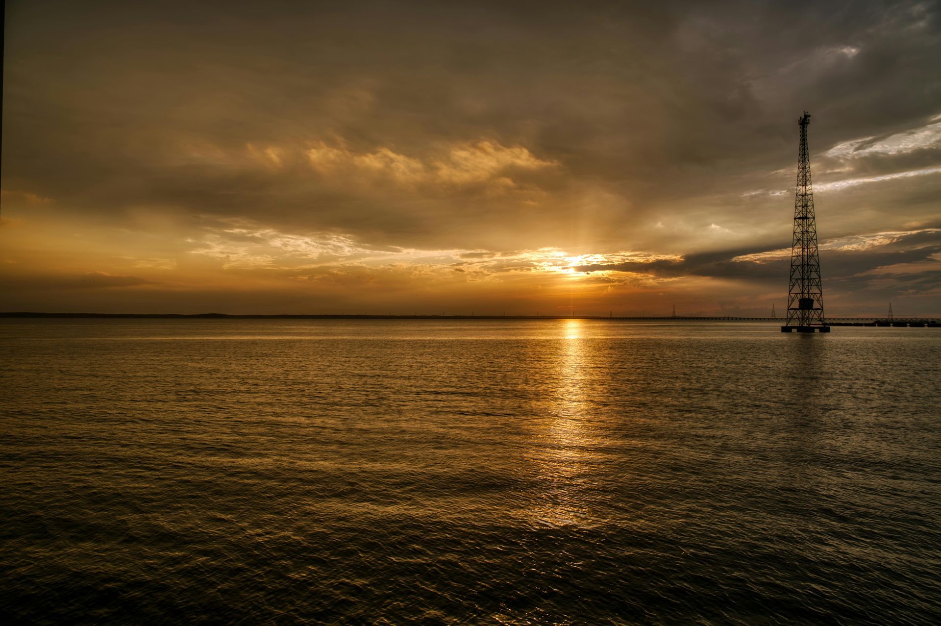 A sunset over a large body of water with a tower in the distance.