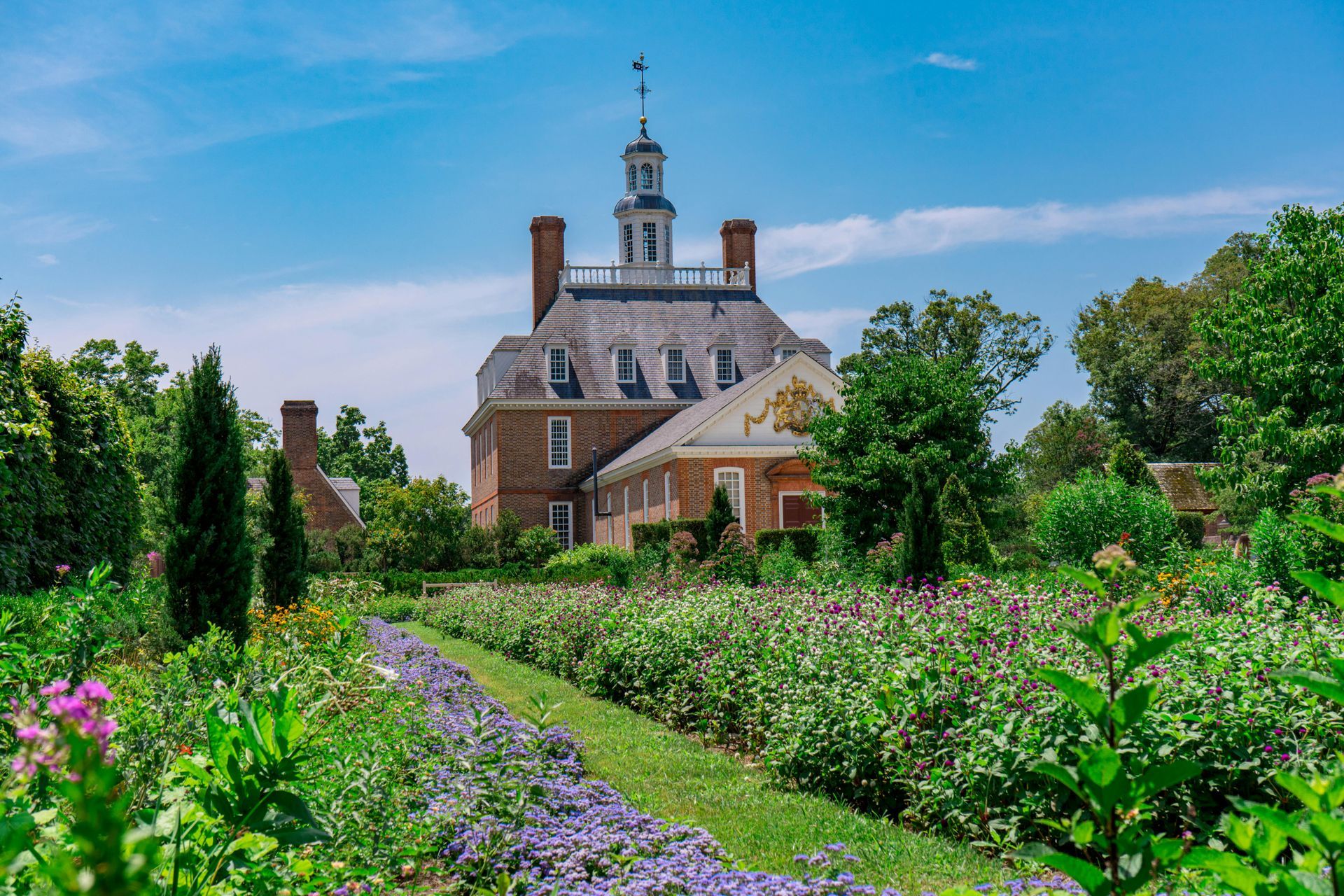 A large house with a clock tower is surrounded by flowers and trees.