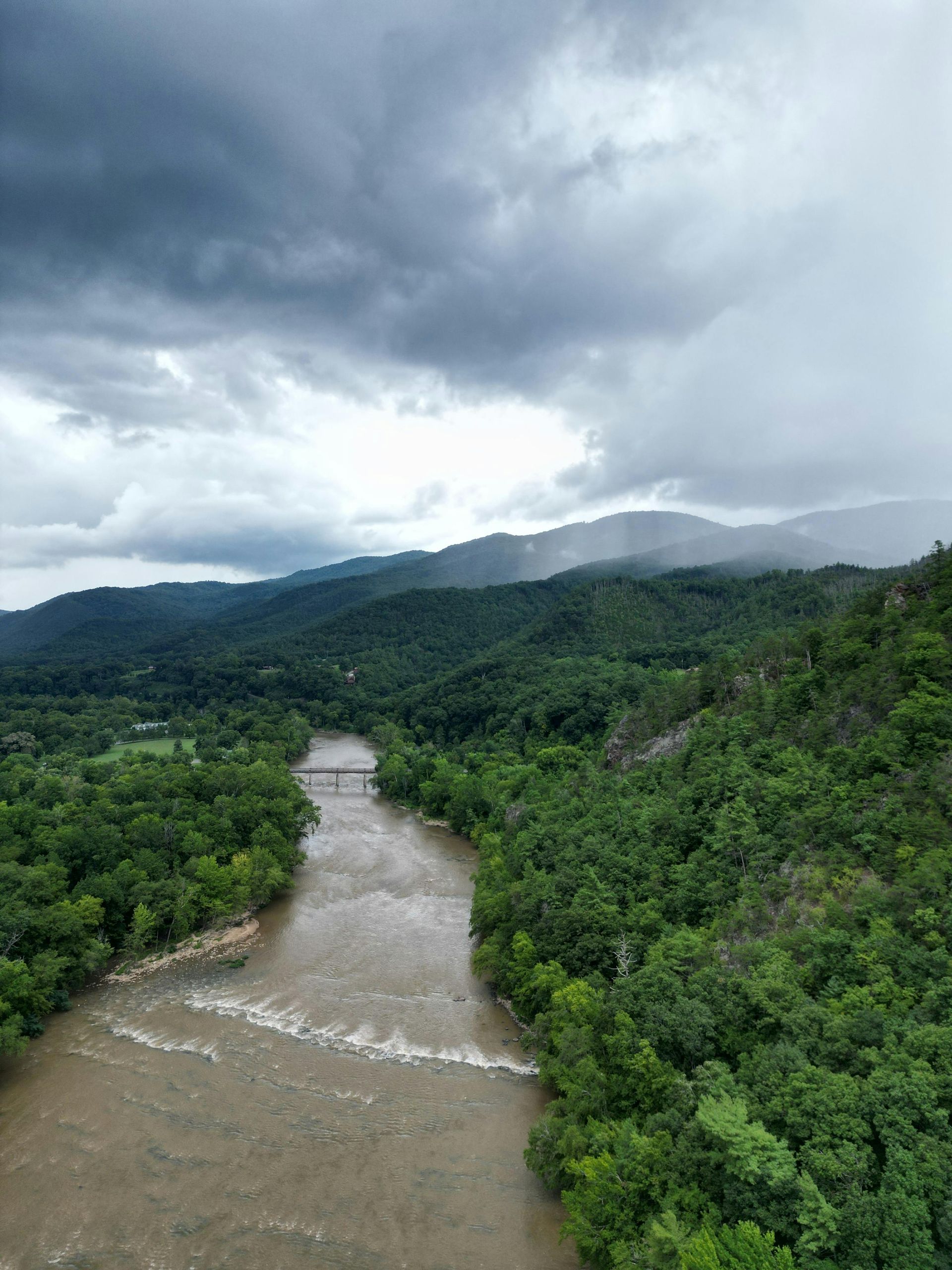 An aerial view of a river surrounded by trees and mountains on a cloudy day.