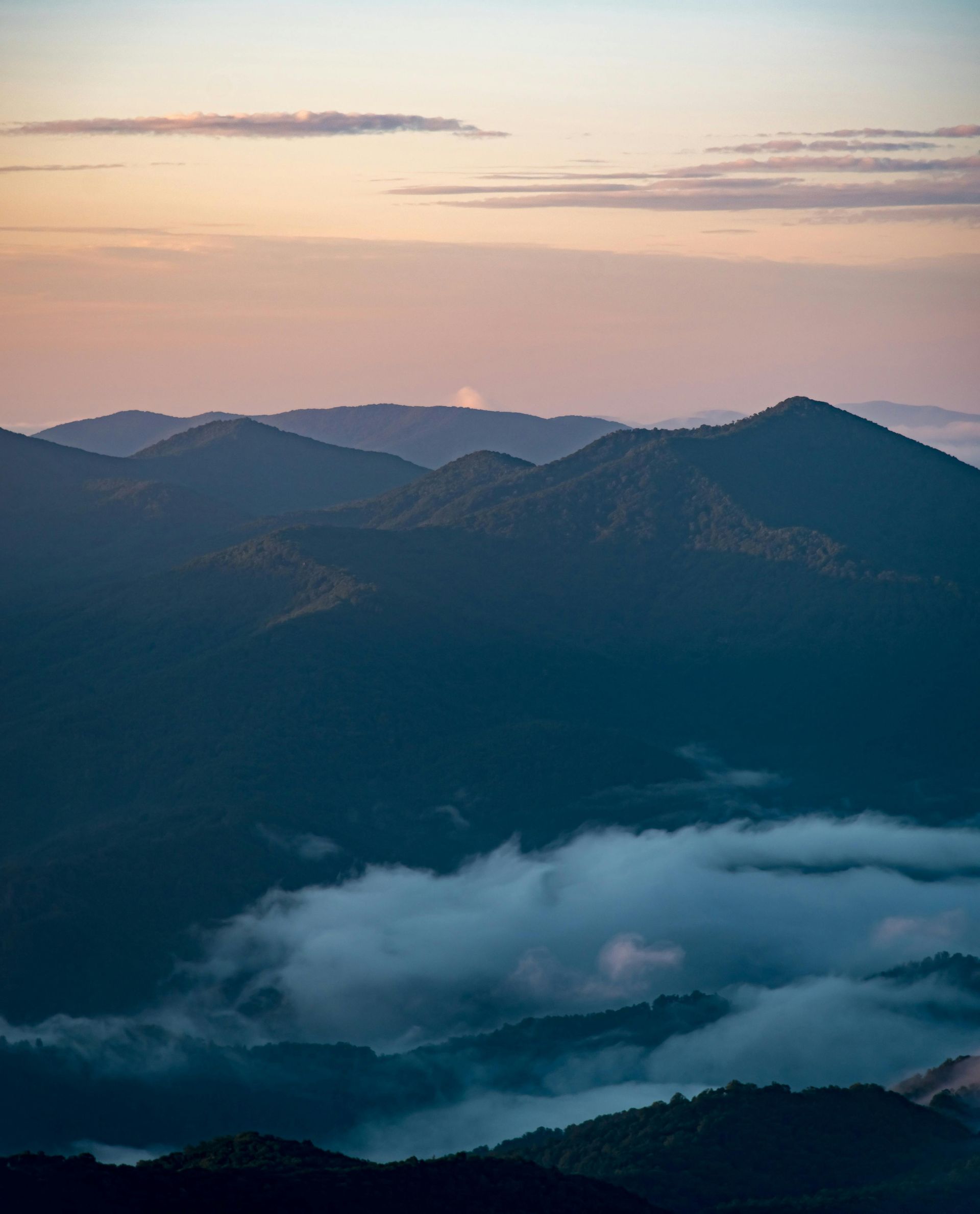 A view of a mountain range at sunset with clouds in the foreground.