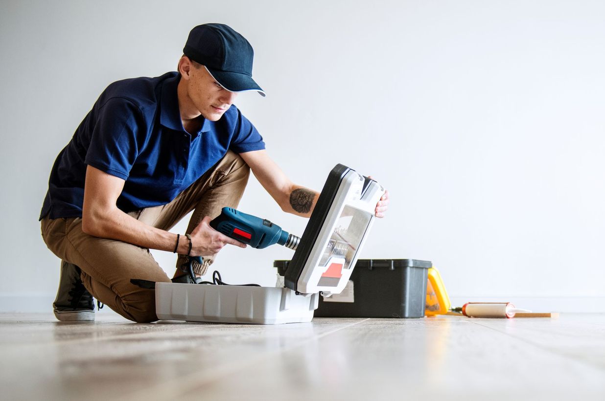 A man is kneeling down on the floor holding a drill.