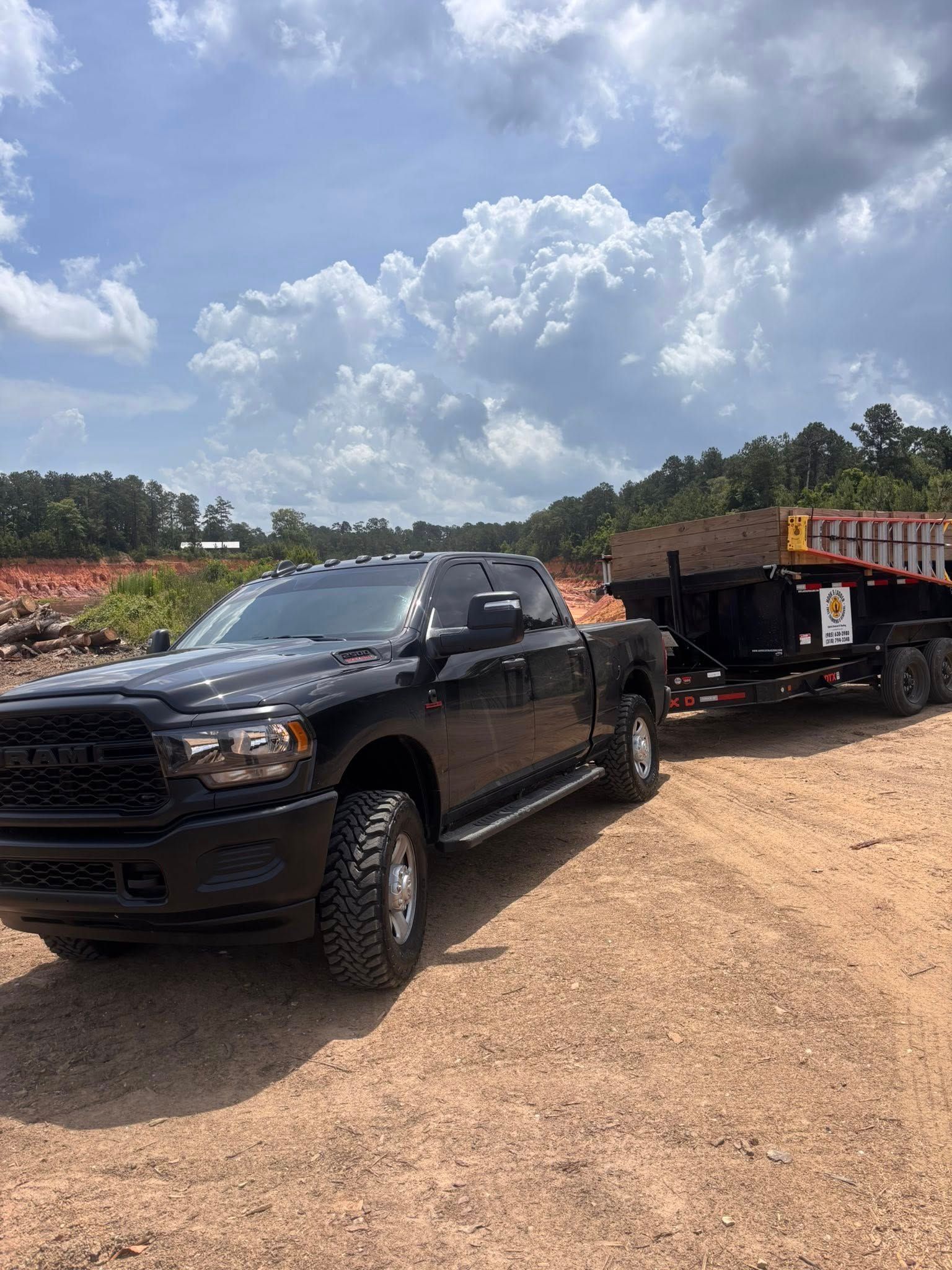 A black Ram heavy-duty pickup truck parked on a gravel lot, hitched to a large flatbed equipment trailer.