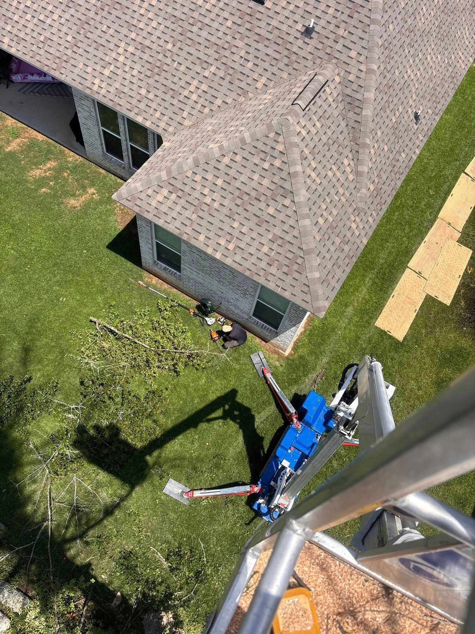A high-angle view shows a worker near a house, with a blue hydraulic lift parked on the grass below.