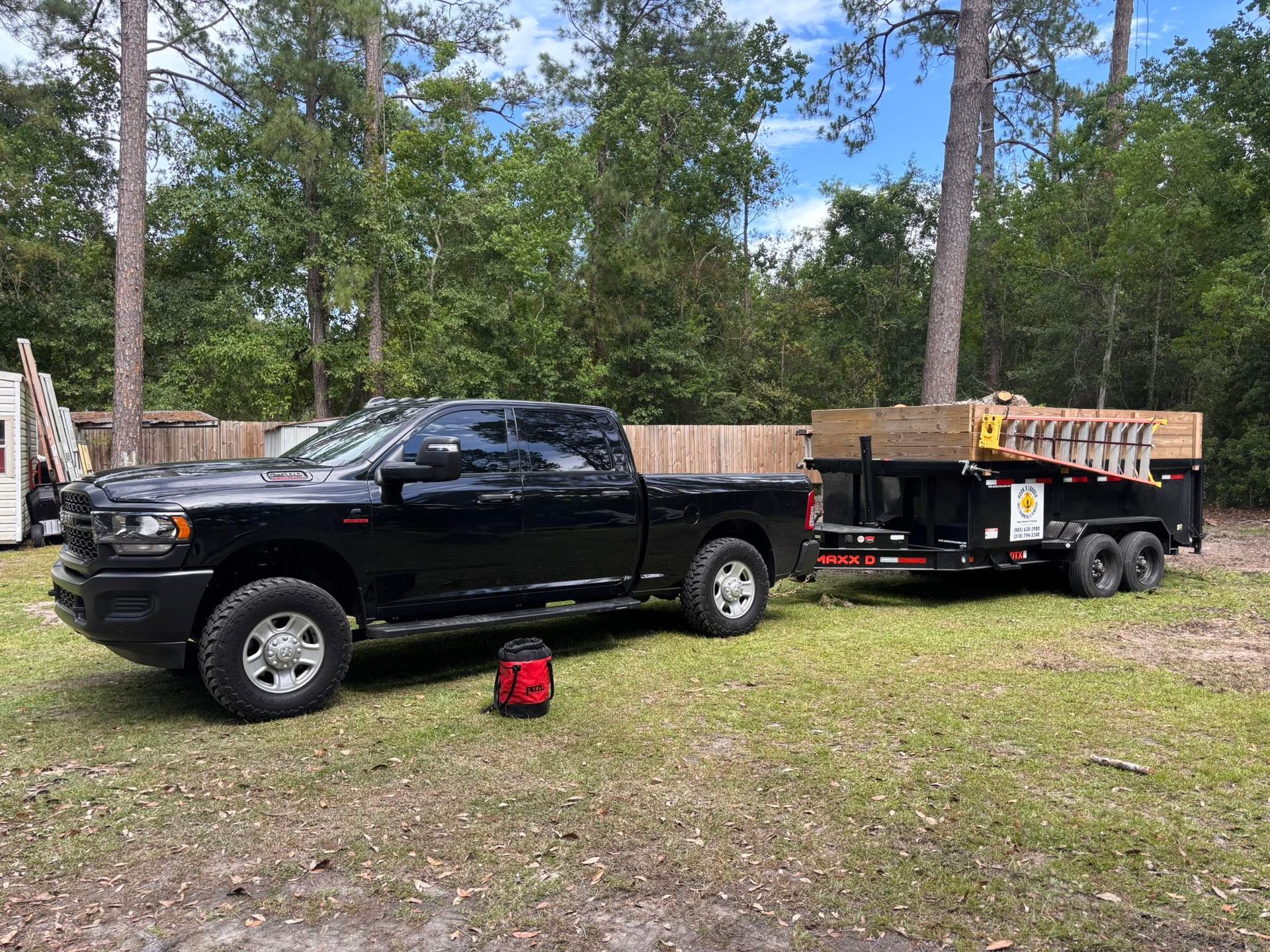 A black pickup truck parked on grass is hitched to a black utility trailer loaded with equipment and a ladder.