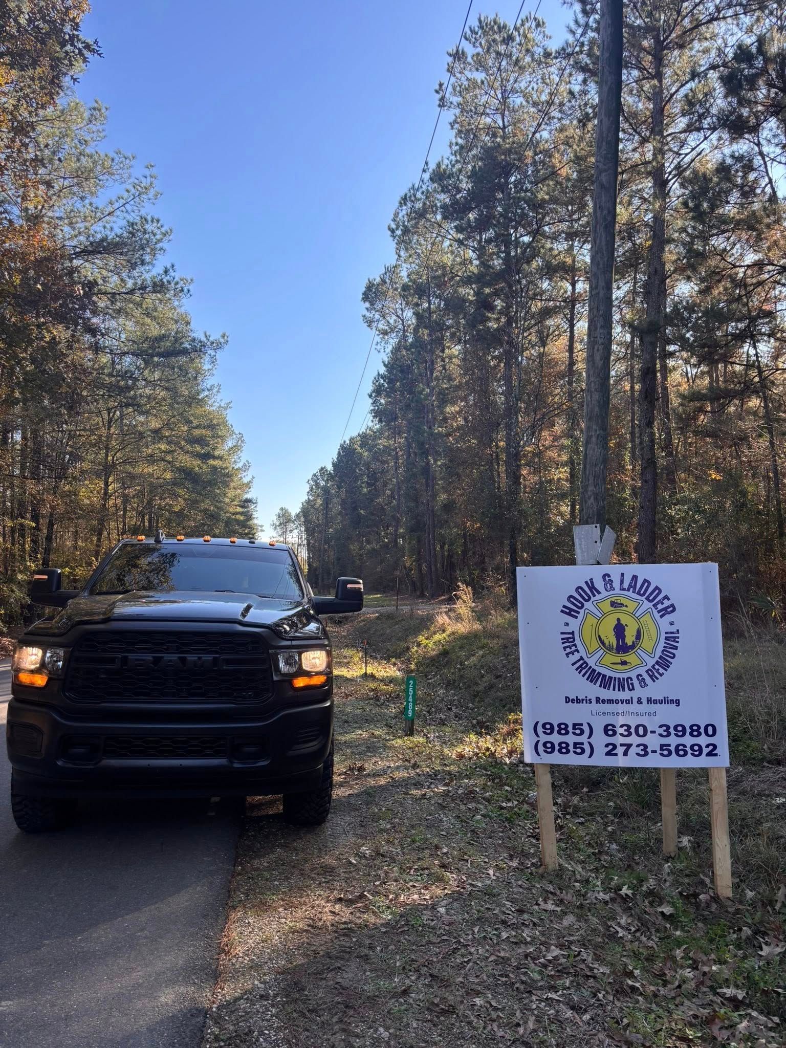 A black pickup truck parked on the shoulder of a road next to a sign for a local landscaping business.