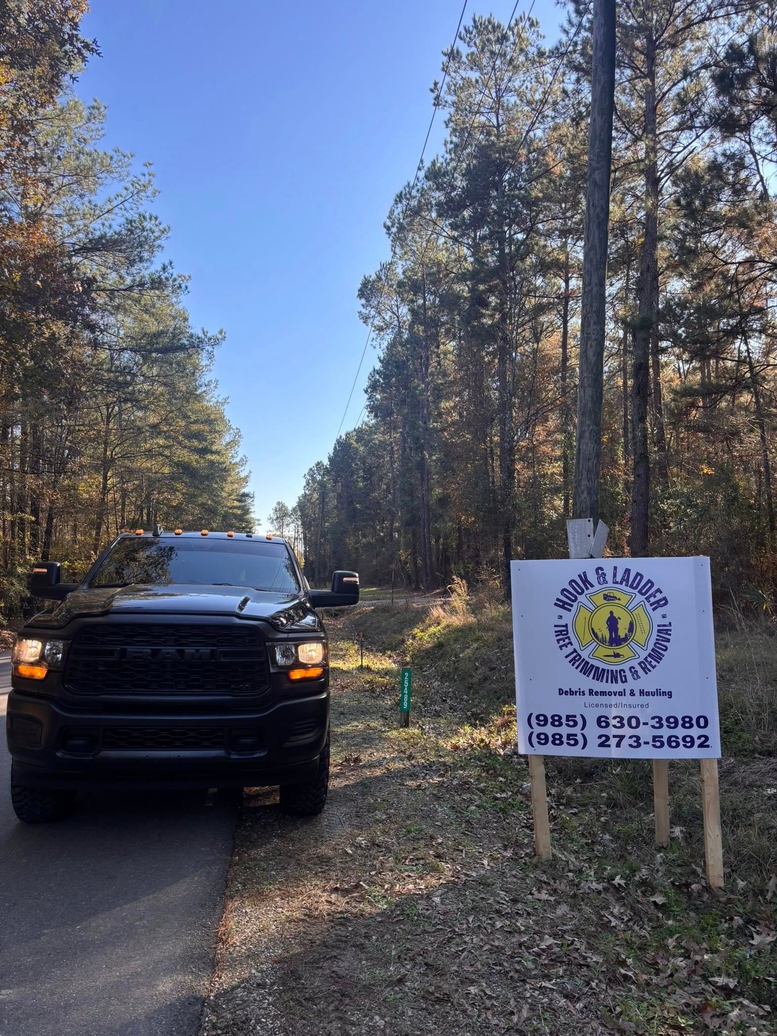 A black Ram pickup truck is parked on the side of a road next to a white sign in a wooded area.
