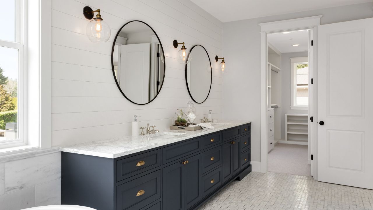 A bathroom with two sinks , two mirrors and a walk in closet.