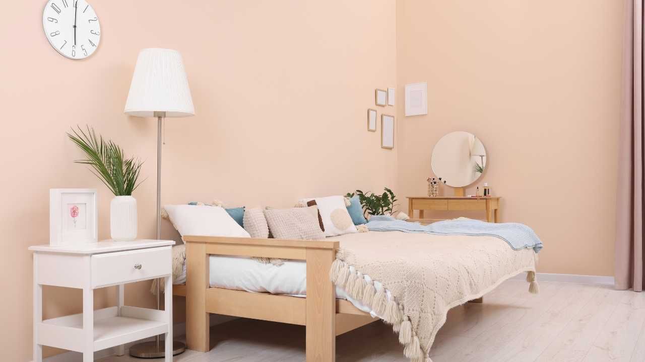 A bedroom with a pink wall, couch , lamp , and mirror.