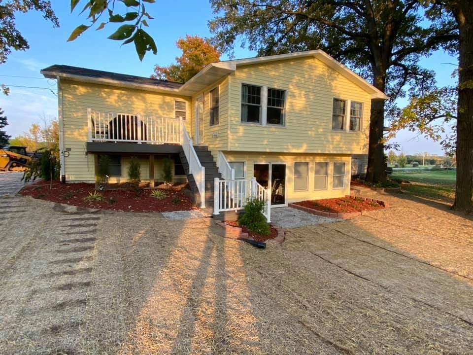 Yellow two-story house with porch, stairs, and gravel driveway at sunset