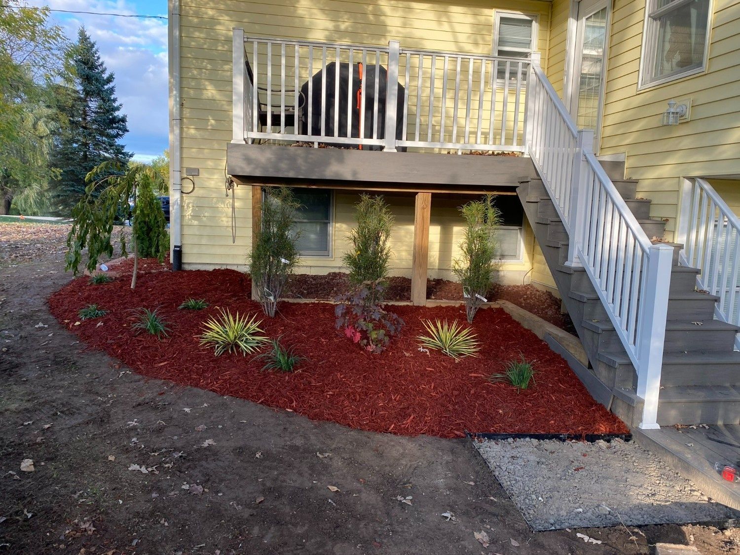 Yellow house exterior with porch, white stairs, and red mulch landscaping below