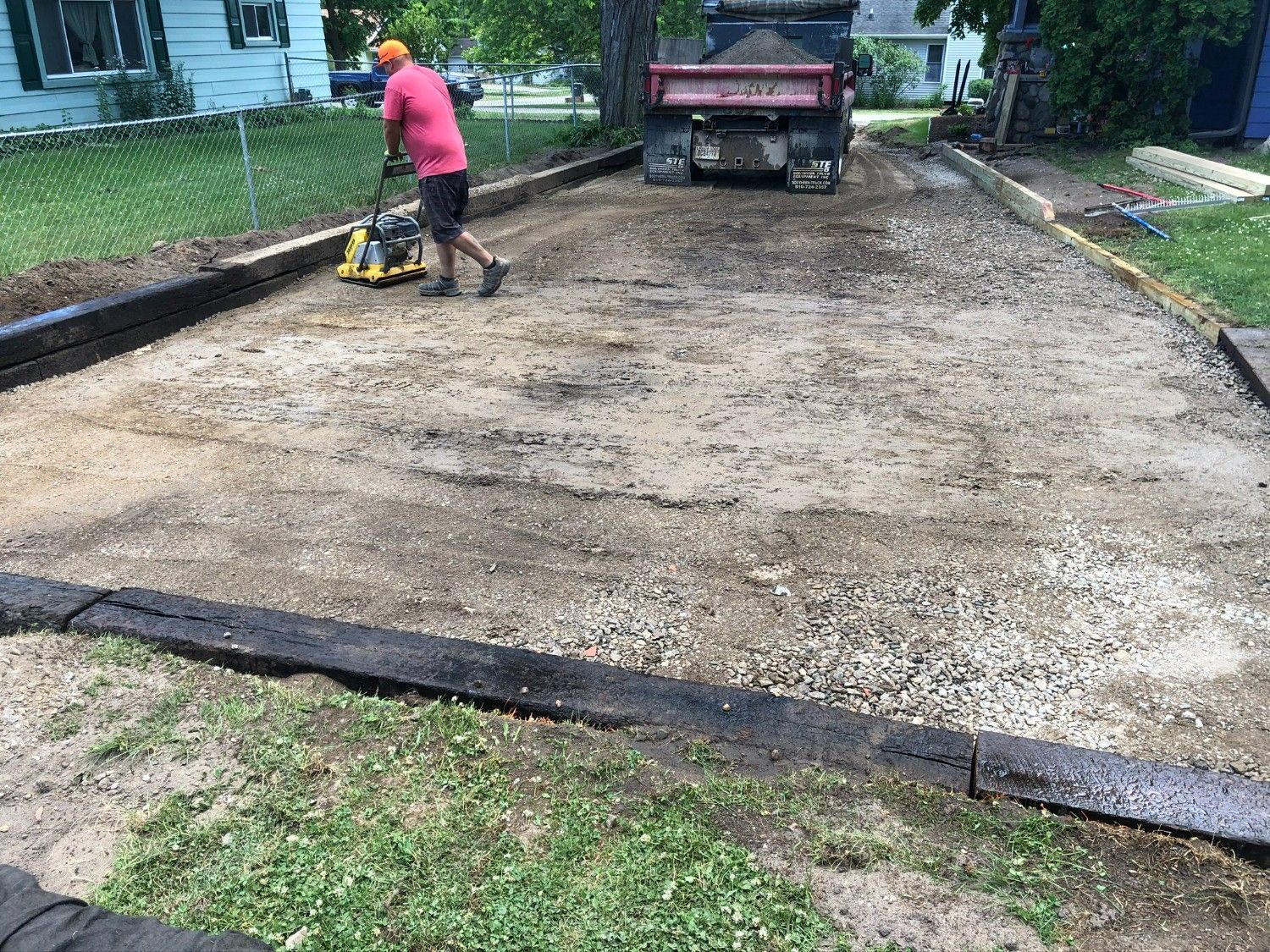 Worker compacting a gravel driveway with a plate compactor beside a truck