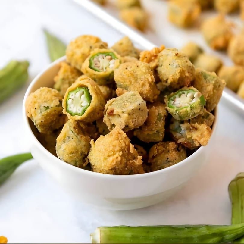 Bowl of crispy fried okra pieces, some showing green centers, on a light background