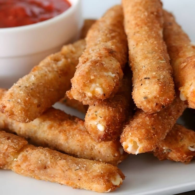 Golden fried mozzarella sticks with marinara dipping sauce in a white bowl