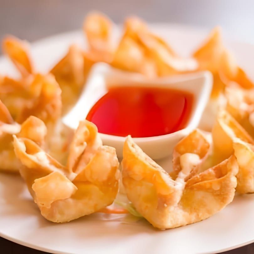 Crispy fried dumplings arranged around a bowl of red dipping sauce on a white plate