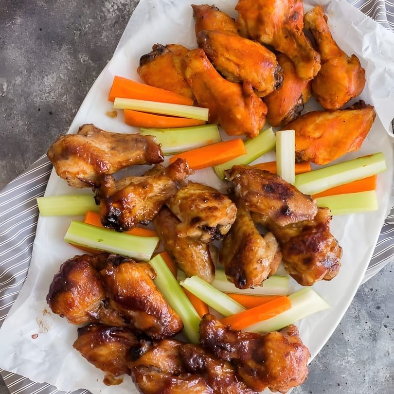 Assorted buffalo chicken wings with celery and carrot sticks on a white paper-lined tray