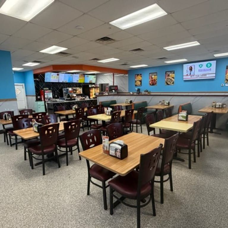 Empty casual dining area with tables, chairs, blue walls, and menu screens above the counter