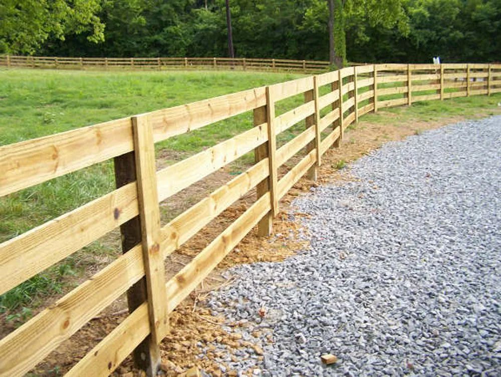 A wooden fence surrounds a grassy field and gravel road.